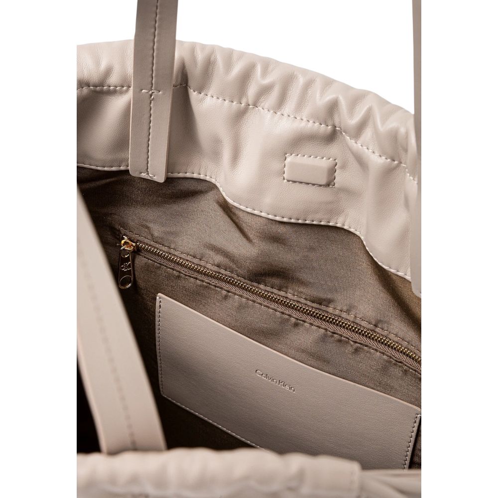This Tote Handbag by Calvin Klein for women in polyethylene & polyurethane and beige presents a sculptural silhouette featuring a secure drawstring, ample , and versatile handle for a sculptural finish.