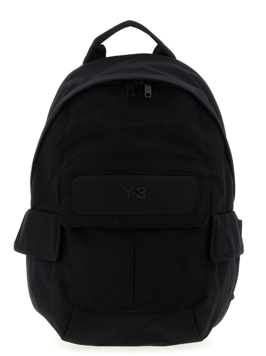 Small Flap Backpack by Y-3 for unisex in coated canvas black features an stately silhouette from the Cordura Coated Canvas Small Flap Backpack range, with a secure flap, zipper & magnetic, ample external-pockets, and versatile backpack-strap, adjustable-strap & handle.